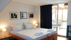 A bedroom with a large bed, wooden headboard, and a sliding glass door leading to a balcony with outdoor furniture. - Pension Bella Vista (Bochum)