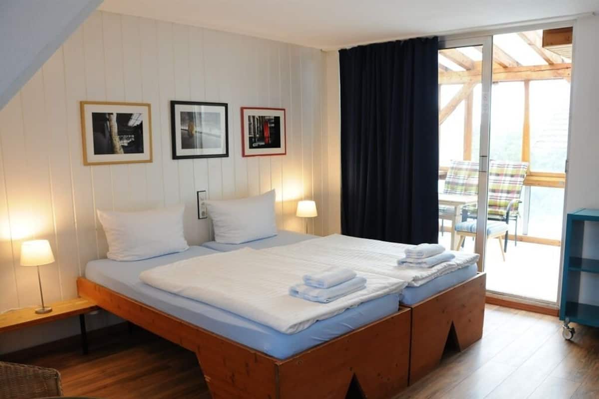 A bedroom with a large bed, wooden headboard, and a sliding glass door leading to a balcony with outdoor furniture.