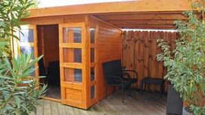 A wooden cabin with a sliding door, a small table, two chairs, and a potted plant. - Pension Bella Vista (Bochum)