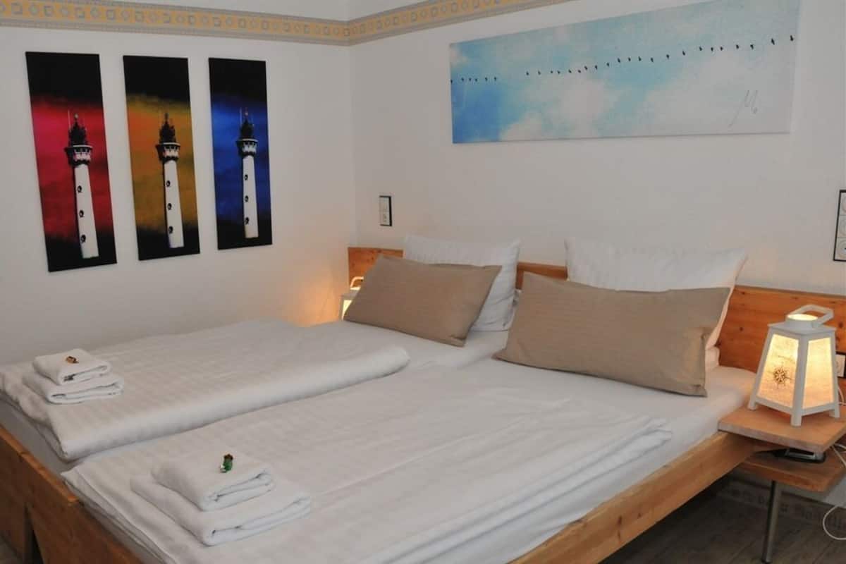 A double bed with white linens and a nightstand with a lamp.