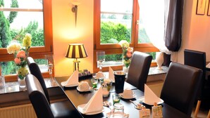 A dining table set for four with chairs, a lamp, and a view of greenery outside. - Pension Bella Vista (Bochum)