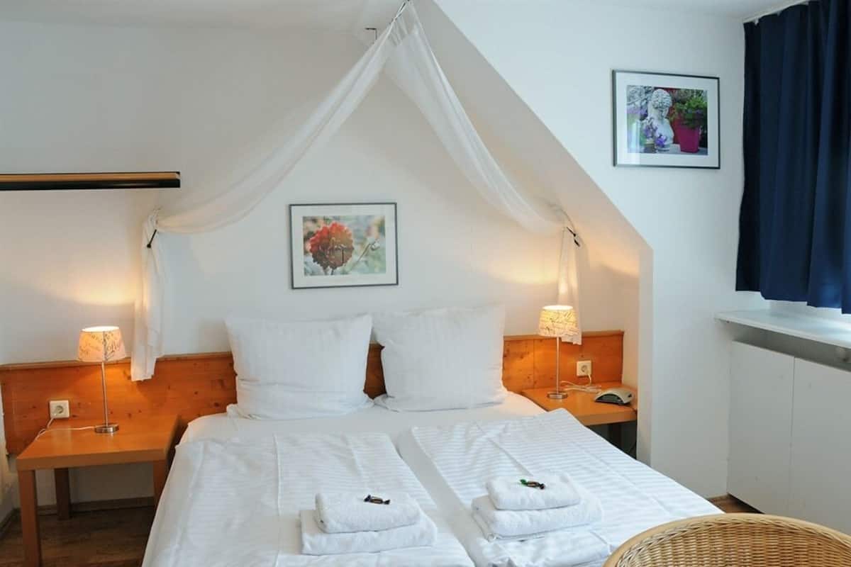 A bedroom with a canopy bed, two bedside lamps, a wicker chair, and a framed picture on the wall.