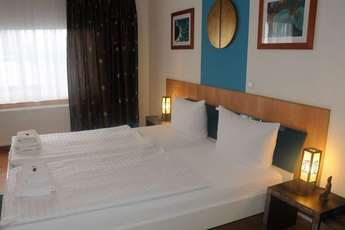 A double bed with white linens, a headboard, bedside lamps, and a small table with a lamp.