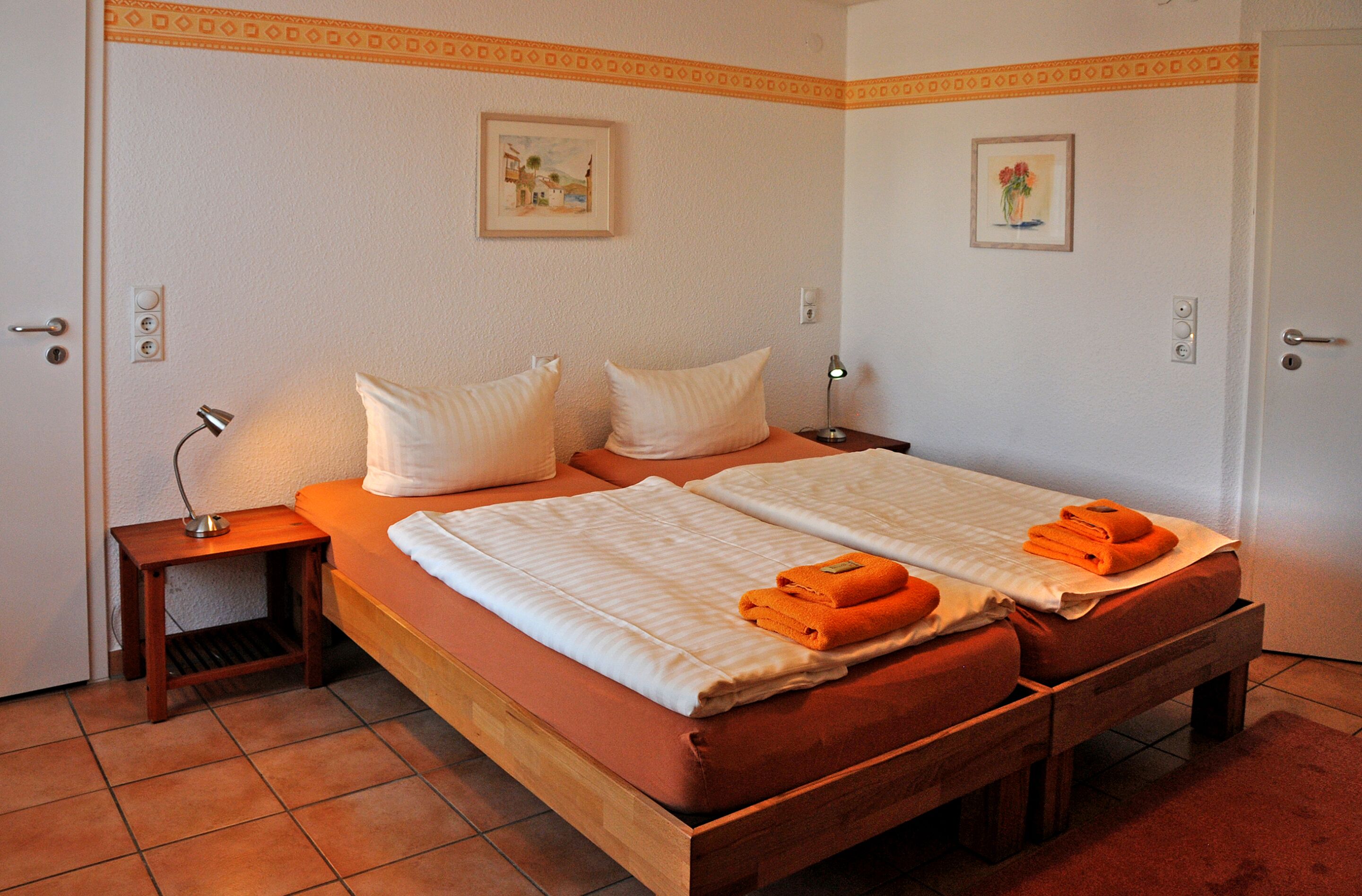 A double bed with two pillows, a bedside table with a lamp, and a small shelf.
