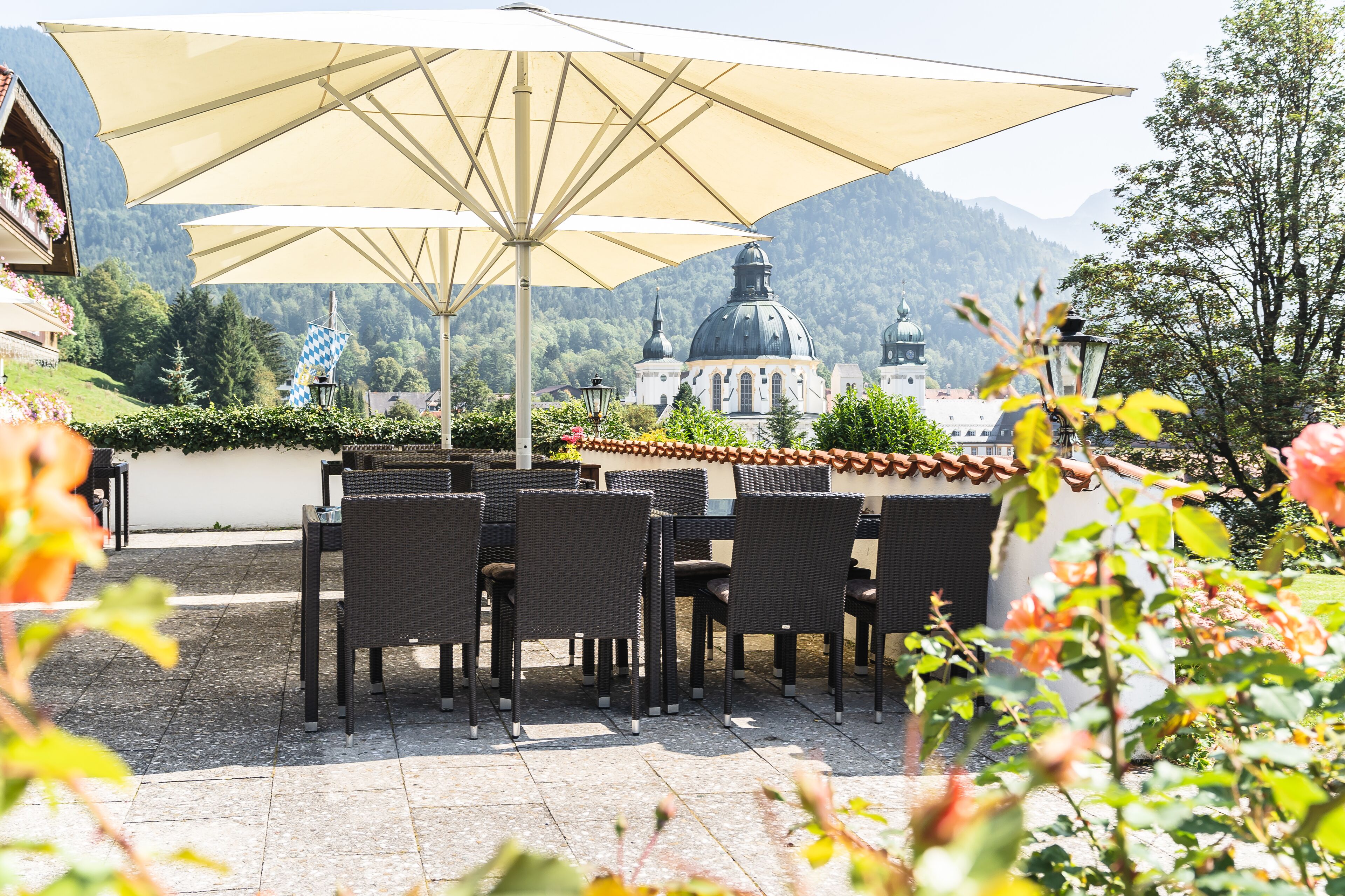An outdoor patio with wicker tables and chairs, a large umbrella, and a view of a building with domed architecture in the background.