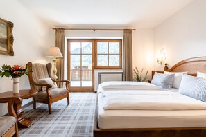 A hotel room with a bed, a chair, a table, a lamp, and a window with curtains. - Hotel Blaue Gams (Ettal)