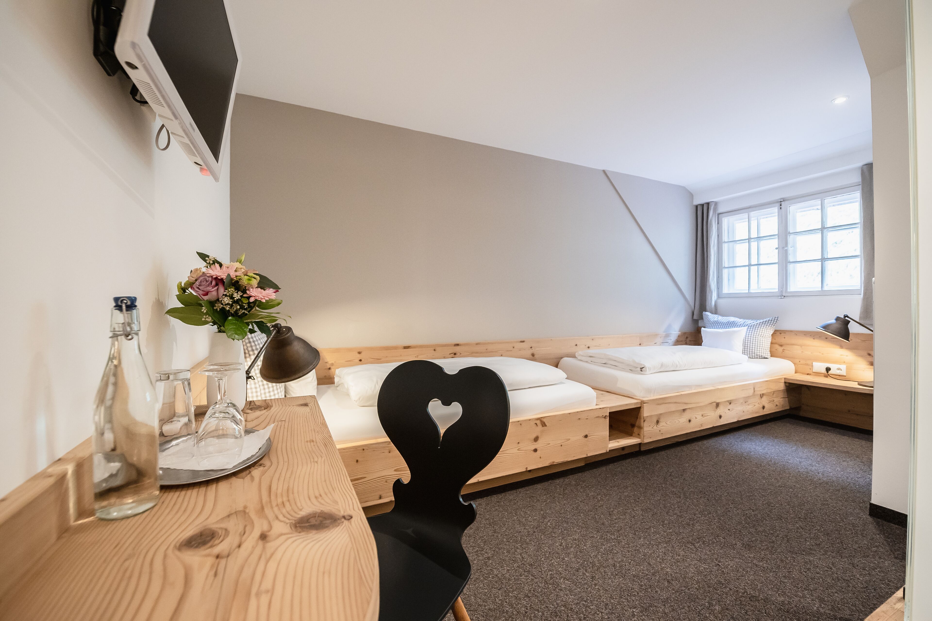 Ein modernes Hotelzimmer mit einem hölzernen Bett, einem Schreibtisch mit Blumenvase und einem flachbildfernseher an der Wand.