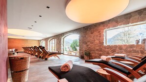 Une salle de spa dotée de plusieurs tables de massage, de murs en pierre et de grandes fenêtres offrant une vue sur l’extérieur.