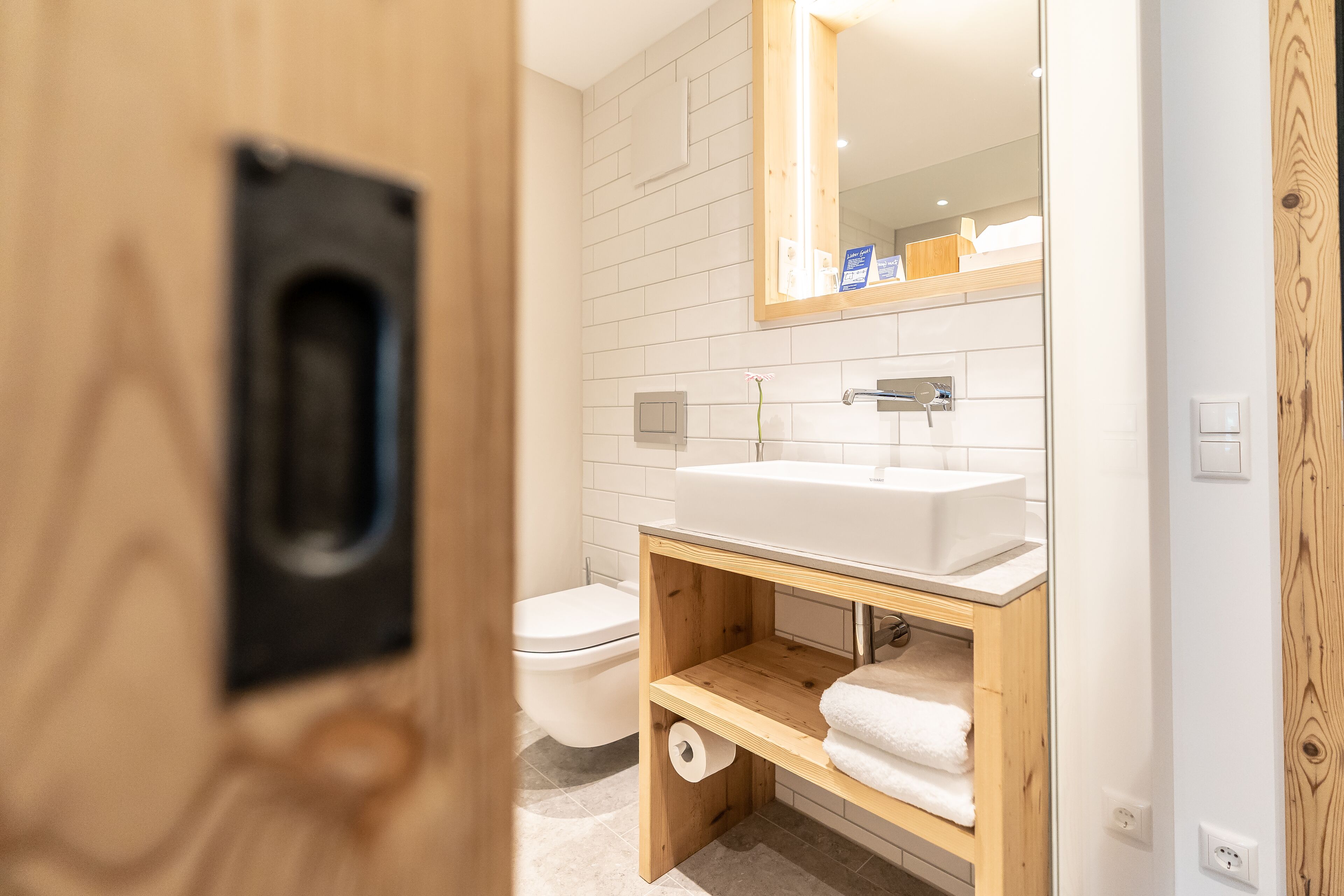 Un baño moderno con un lavamanos blanco, tocador de madera y un espejo encima.