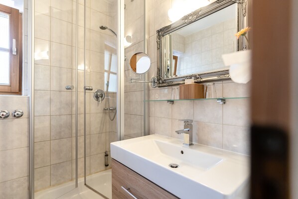 Un baño moderno con cabina de ducha de vidrio, un lavamanos blanco y un espejo grande.
