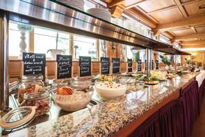 A buffet setup with various food items and labels in a well-lit, wooden interior. - Hotel Blaue Gams (Ettal)