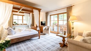 Une chambre à coucher avec un lit à baldaquin, un coin salon avec une table et des fauteuils, et une grande fenêtre avec des rideaux.