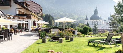 A hotel with outdoor seating, a garden, and a view of a church and mountains.