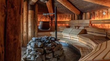 A rustic wooden cabin interior with a stone fireplace, wooden benches, and a hanging pot.