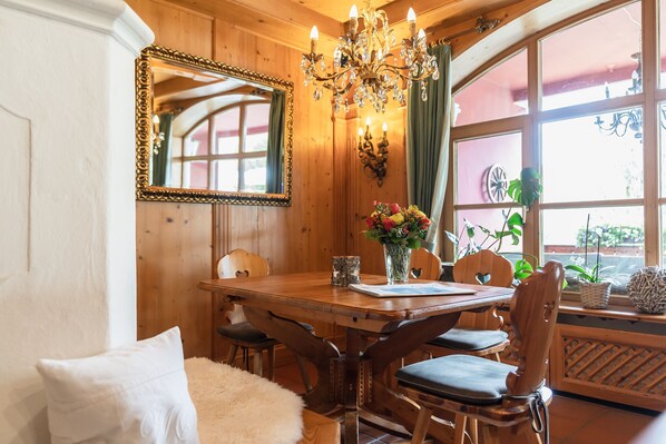 A wooden dining room with a chandelier, a mirror, and a window with plants. - Hotel Blaue Gams (Ettal)