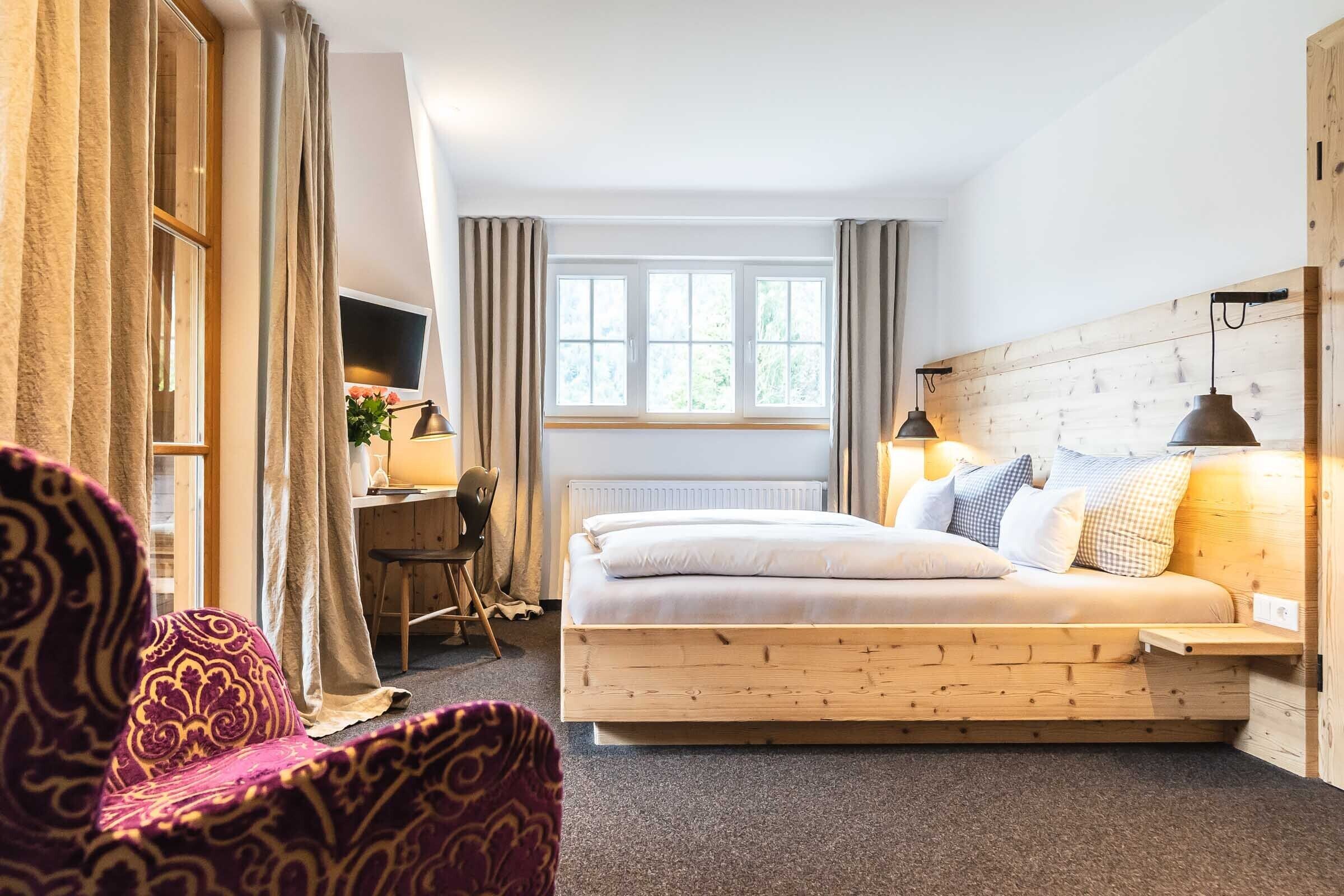A bedroom with a wooden bed, a desk with a chair, a TV, and a window with curtains.