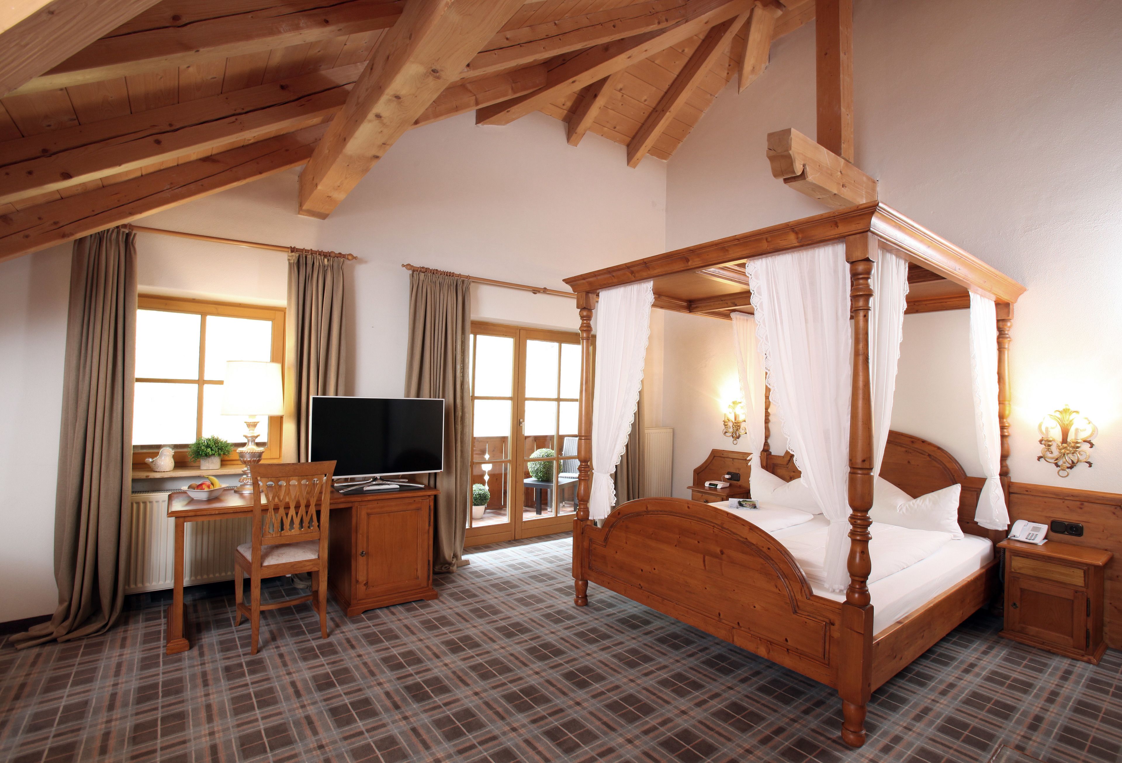 A bedroom with a four-poster bed, a wooden desk with a television, and a chair.