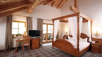 A bedroom with a four-poster bed, a wooden desk with a television, and a chair.
