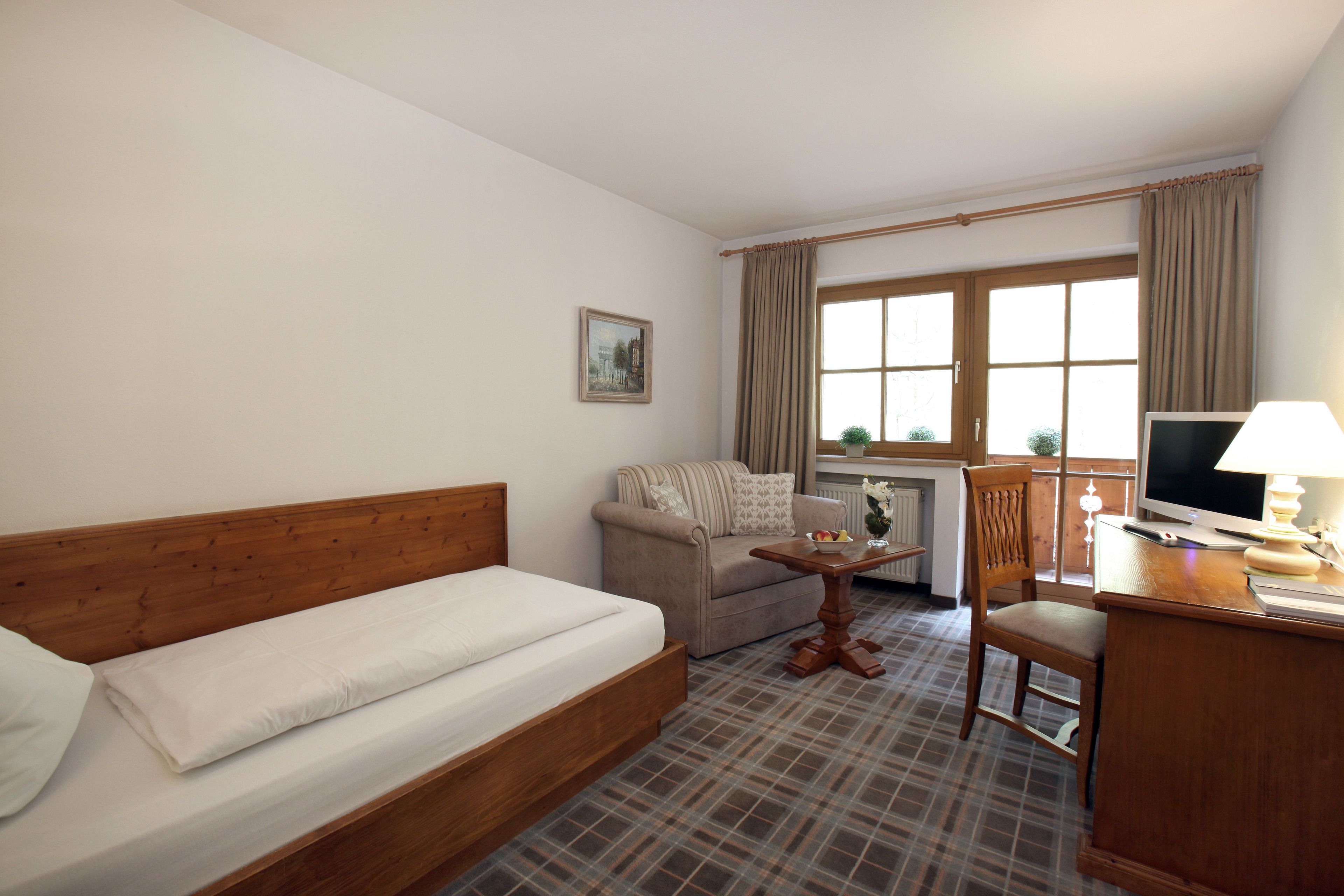 Habitación de hotel con cama, sofá, una mesita, una silla, escritorio con computadora y ventana con cortinas.