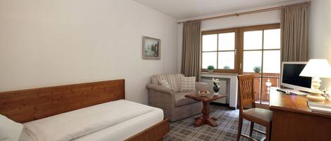 Habitación de hotel con cama, sofá, una mesita, una silla, escritorio con computadora y ventana con cortinas.