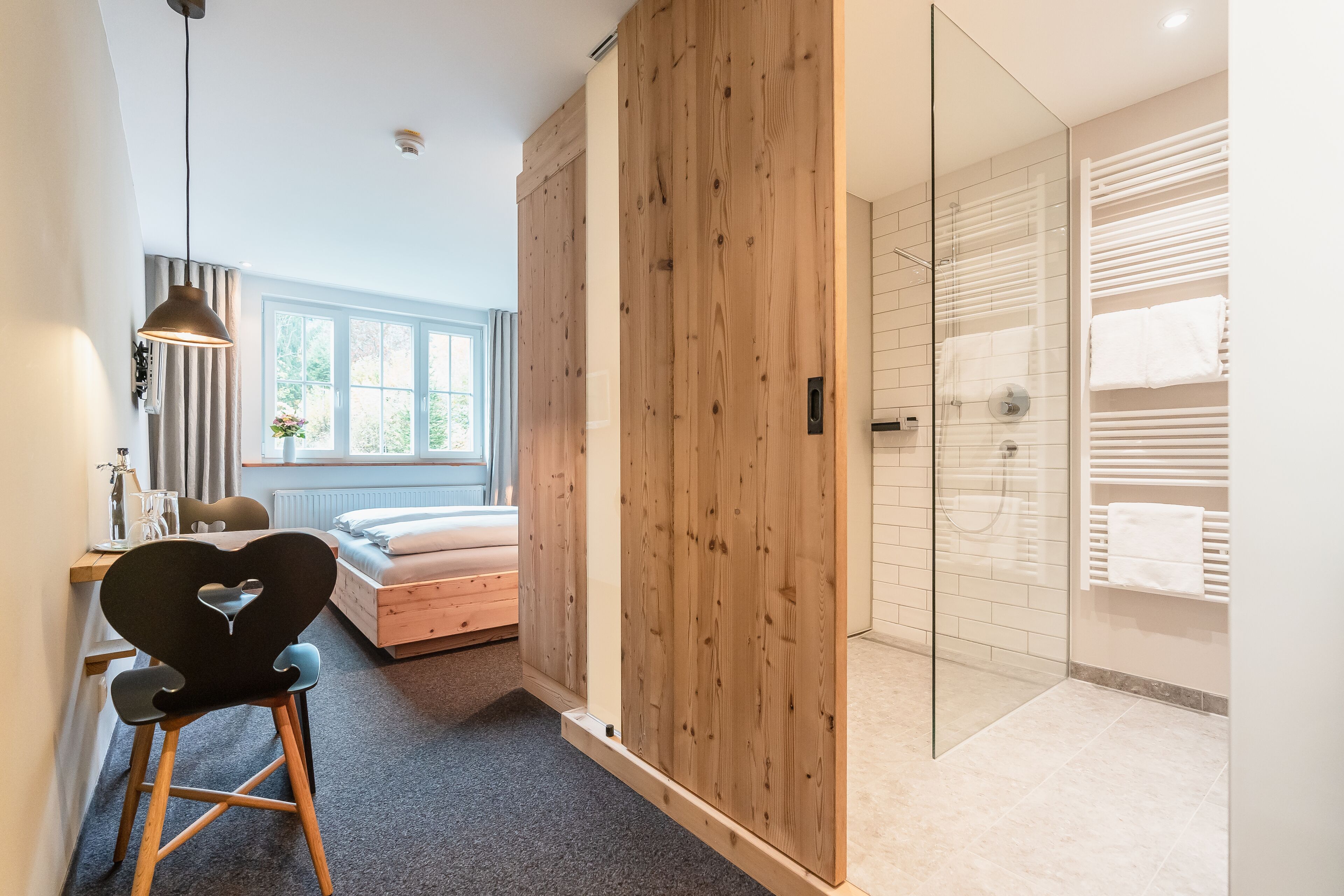 Een slaapkamer met een bed, een bureau, een stoel, een raam en een houten kledingkast.