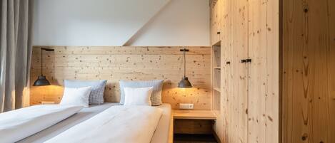 Una habitación de hotel moderna con cabecera de madera, una cama bien tendida con sábanas blancas, dos mesitas de noche con lámparas y un armario de madera.