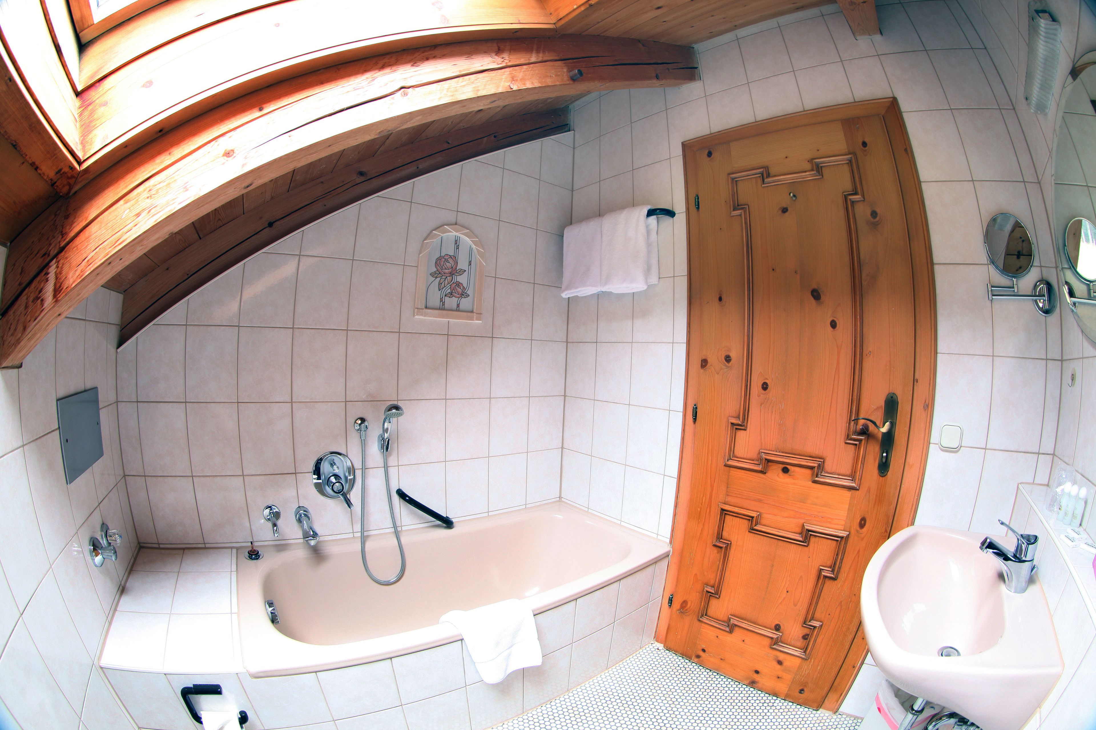 Un bany amb una porta de fusta, una banyera blanca, un lavabo i una dutxera.