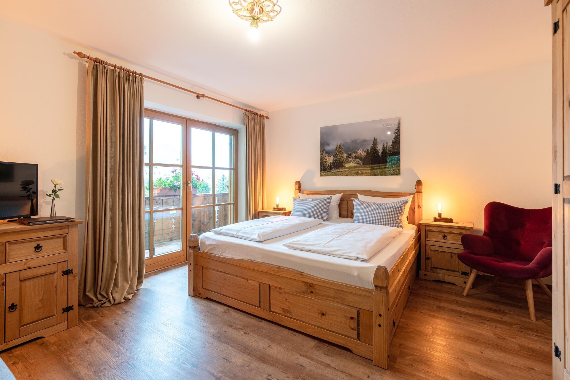 A bedroom with a wooden bed, a red chair, a TV, a nightstand, and a large window.