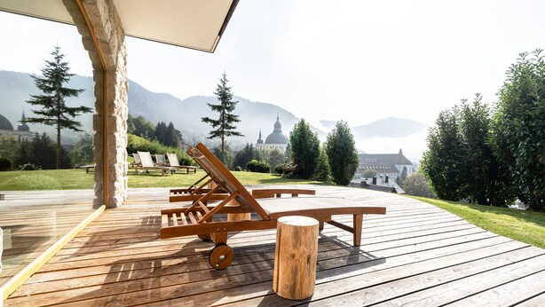 Une terrasse en bois avec des chaises longues et une table, offrant une vue sur un paysage montagneux avec une église.