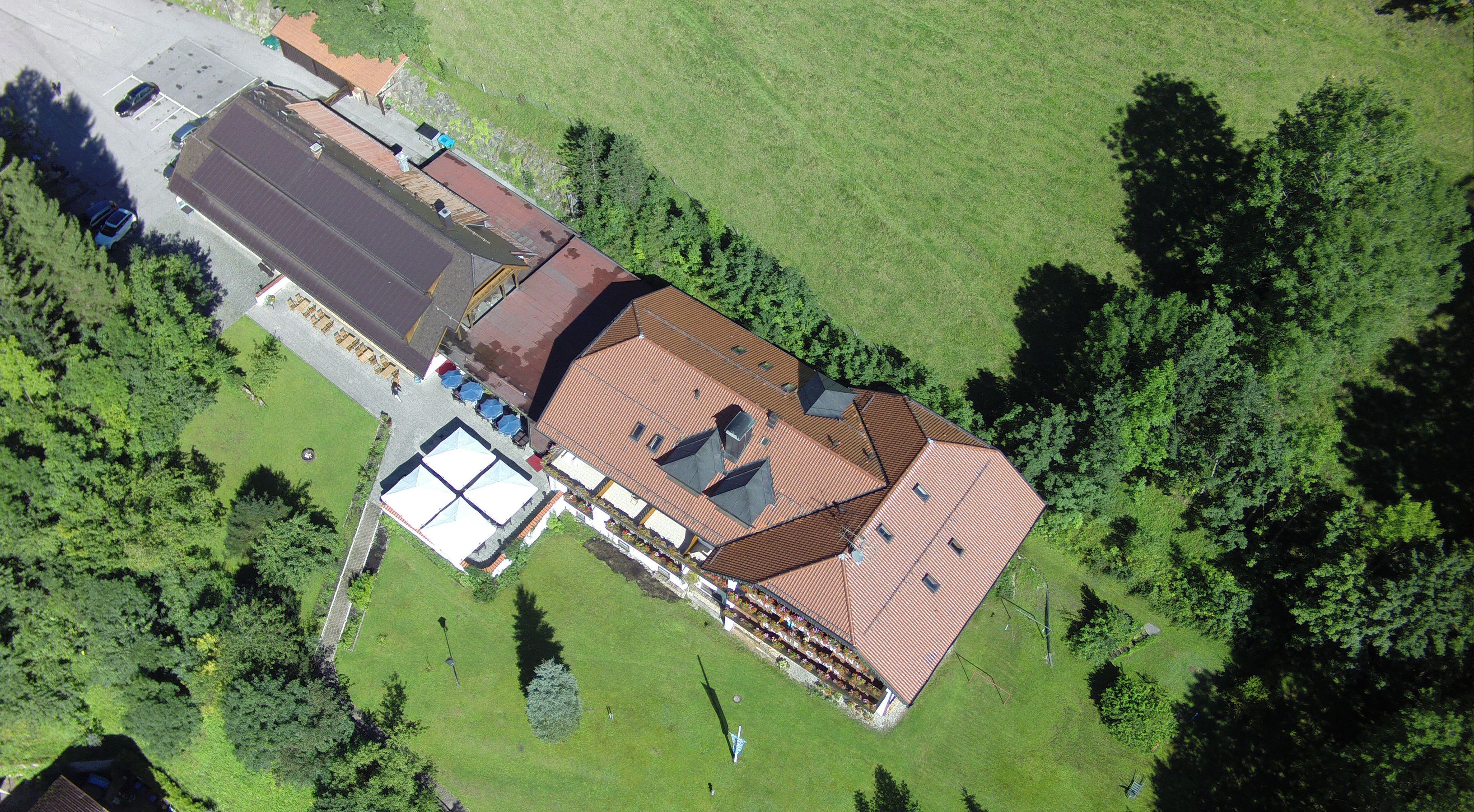 An aerial view of a building with a red-tiled roof, a parking lot, and surrounding green fields.