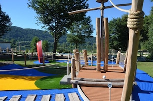 Un parque infantil con una estructura de madera para escalar, cuerdas y una bandera roja.