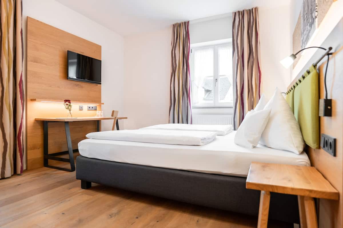 Hotelkamer met een bed, een bureau, een aan een houten paneel bevestigde televisie en een raam met gordijnen.
