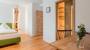 Een moderne slaapkamer met een groen bed, houten vloer en een houten deur naar een eetgedeelte met een tafel en stoel.