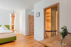 Un dormitorio moderno con cama verde, suelo de madera y puerta de madera que da a un comedor con mesa y silla.