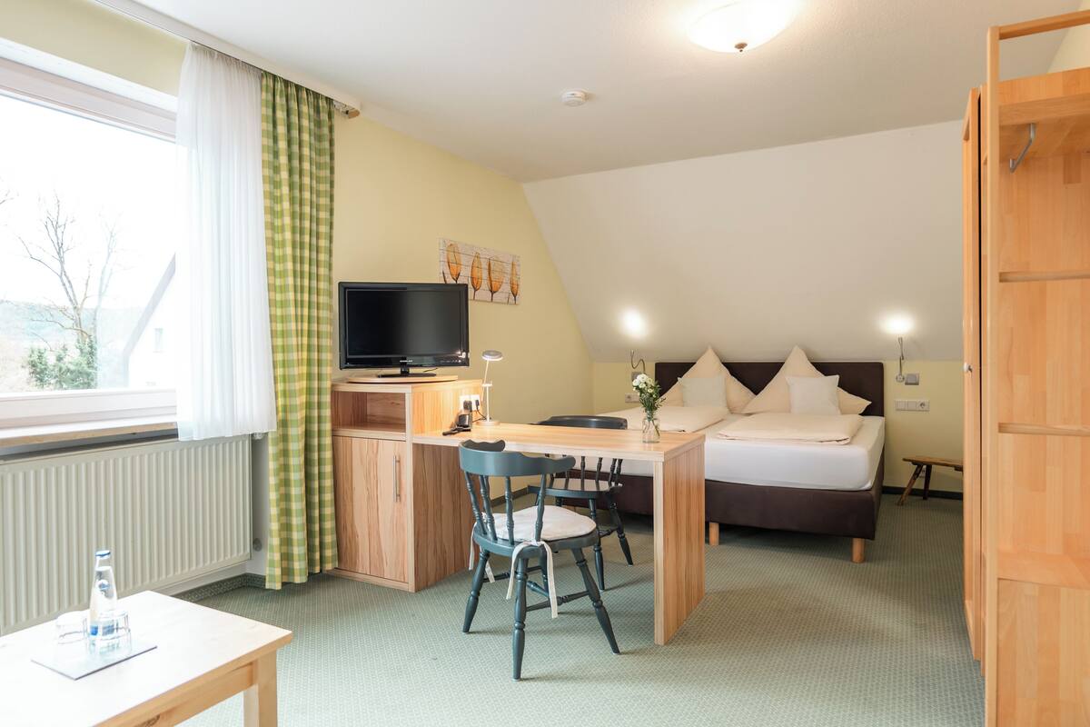 Een slaapkamer met een bed, een bureau, een stoel, een televisie en een raam met gordijnen.