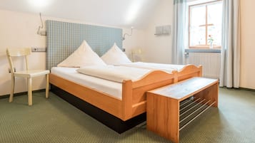 Ein ordentlich eingerichtetes Schlafzimmer mit einem hölzernen Bett, einer Bank, zwei Stühlen und einem Fenster mit Vorhängen.