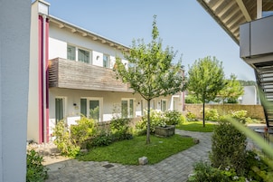 Un edificio moderno de dos pisos con un balcón, un jardín cuidado y un sendero pavimentado.