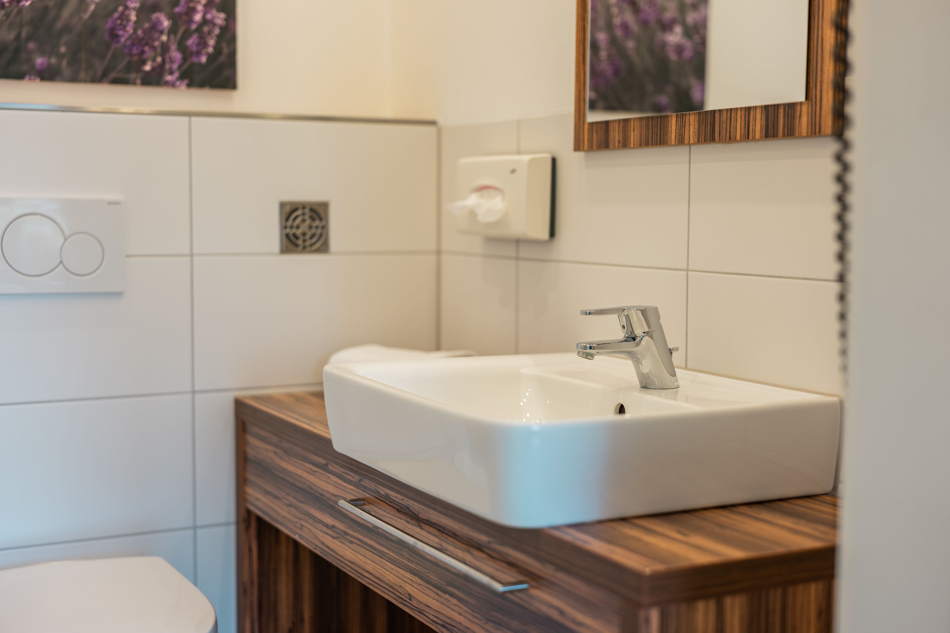 Un baño con lavamanos blanco, tocador de madera y un espejo.