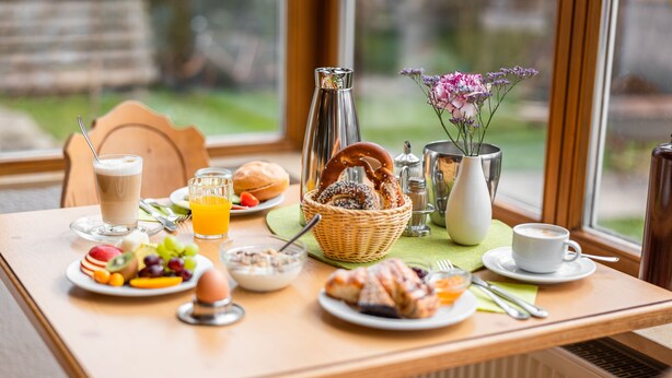 Een ontbijttafel met diverse etenswaren, een koffiekop en een vaas met bloemen.