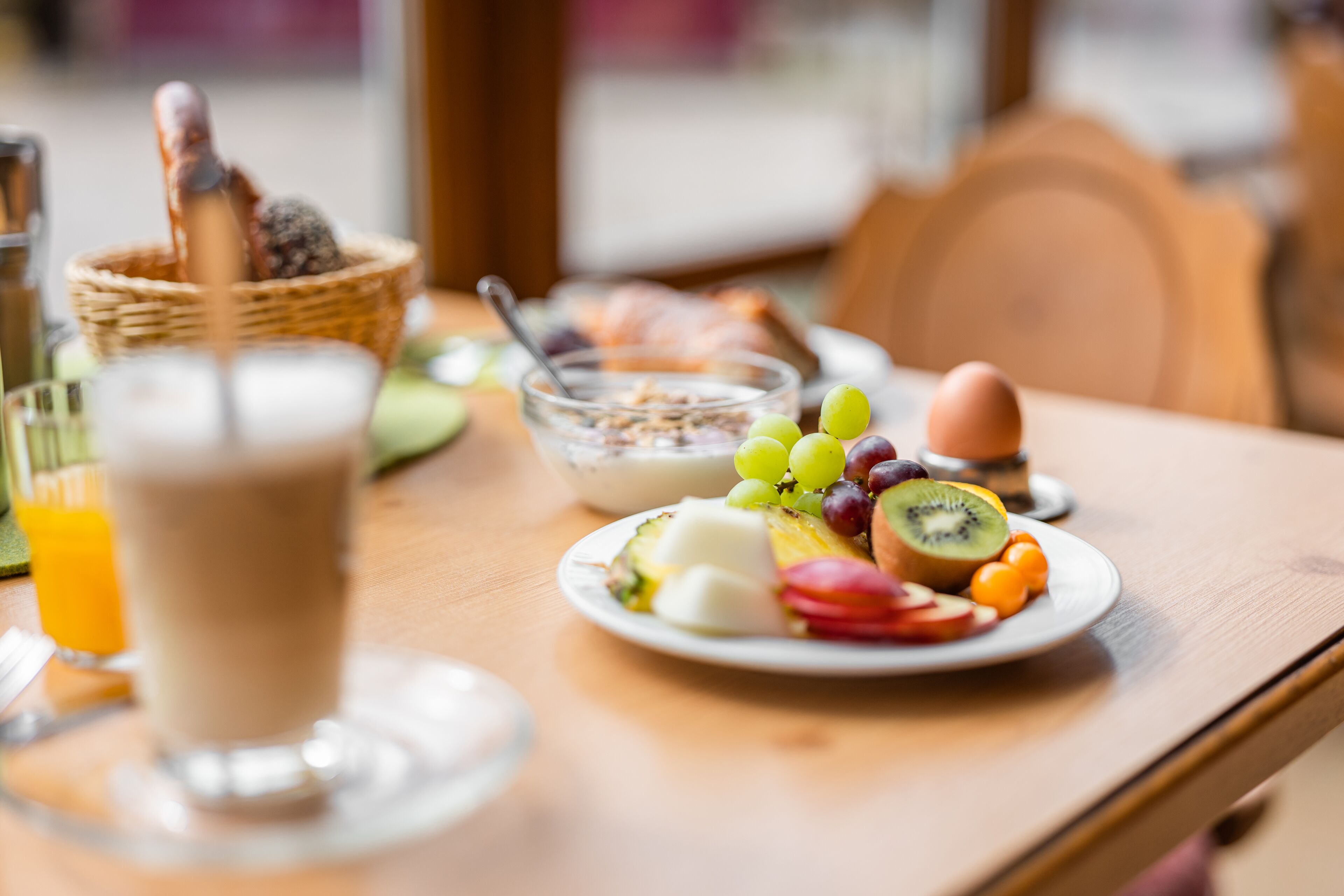 A breakfast table with a plate of fruit, a glass of orange juice, and a bowl of cereal.