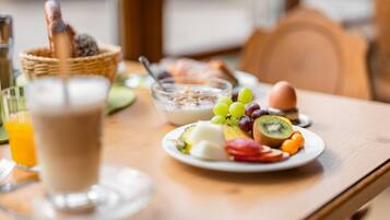 A breakfast table with a plate of fruit, a glass of orange juice, and a bowl of cereal.