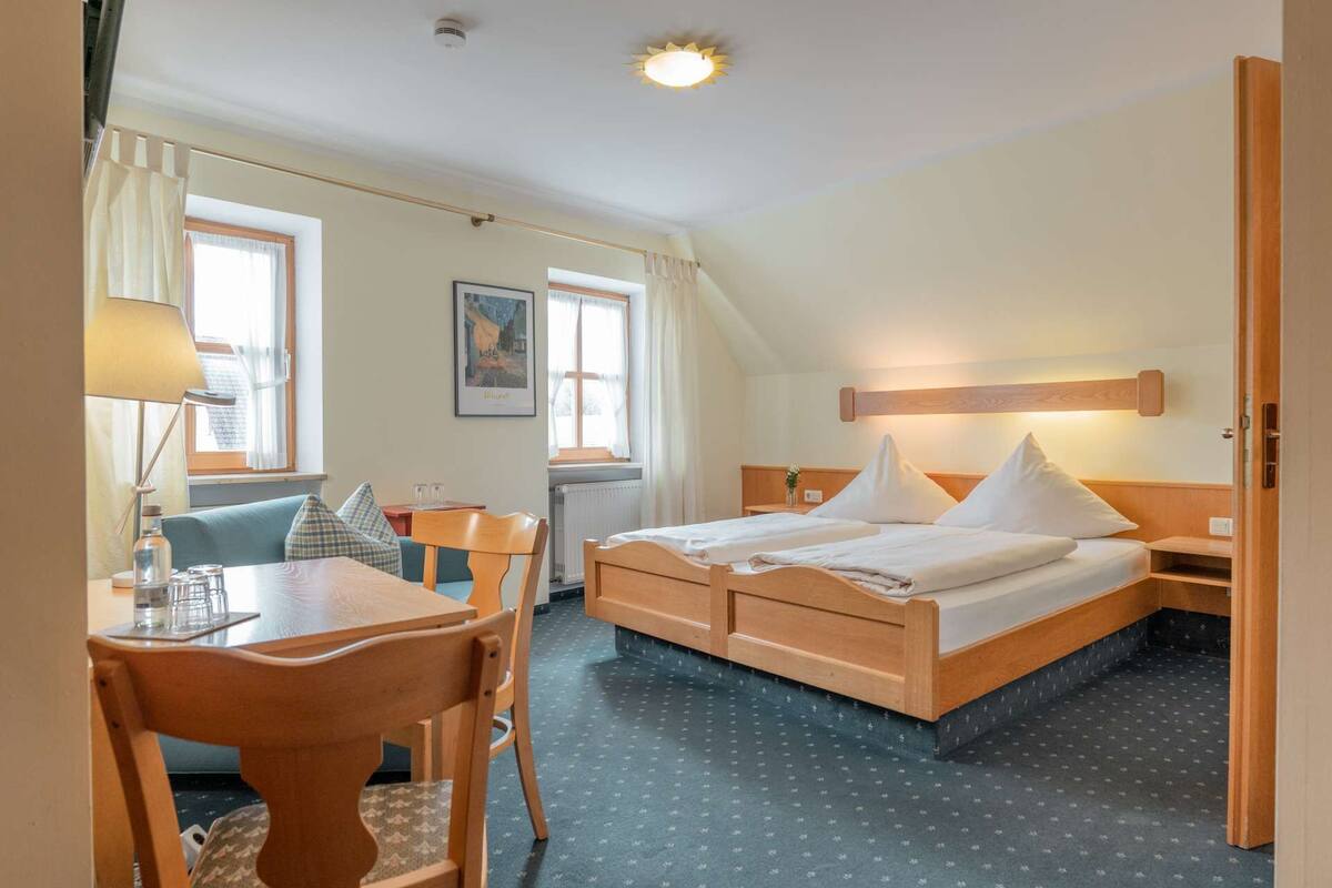 Hotelkamer met een bed, een bureau en een stoel. Er is een raam met gordijnen, een schilderij aan de muur en een plafondlamp.