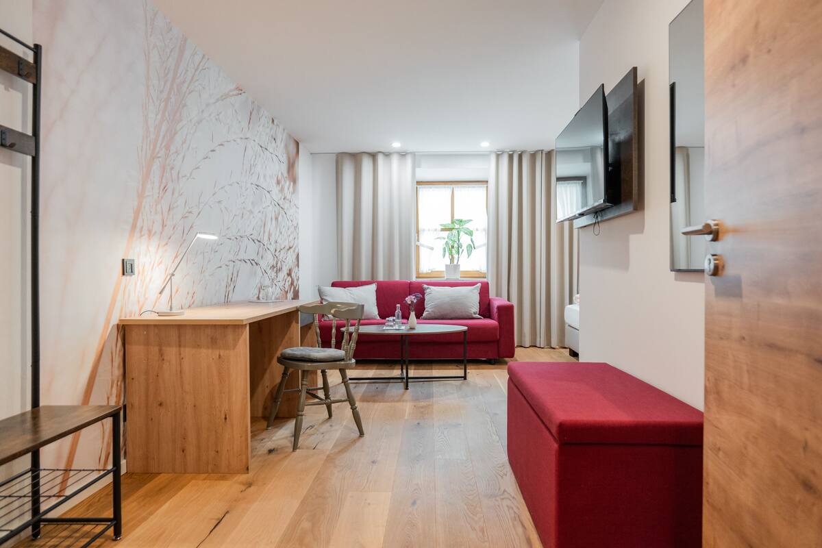 Een moderne woonkamer met een houten bureau, een rode bank, een rode poef en een grote spiegel.