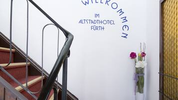 Un escalier avec une rampe métallique et un mur sur lequel est affiché un panneau d’accueil en allemand.