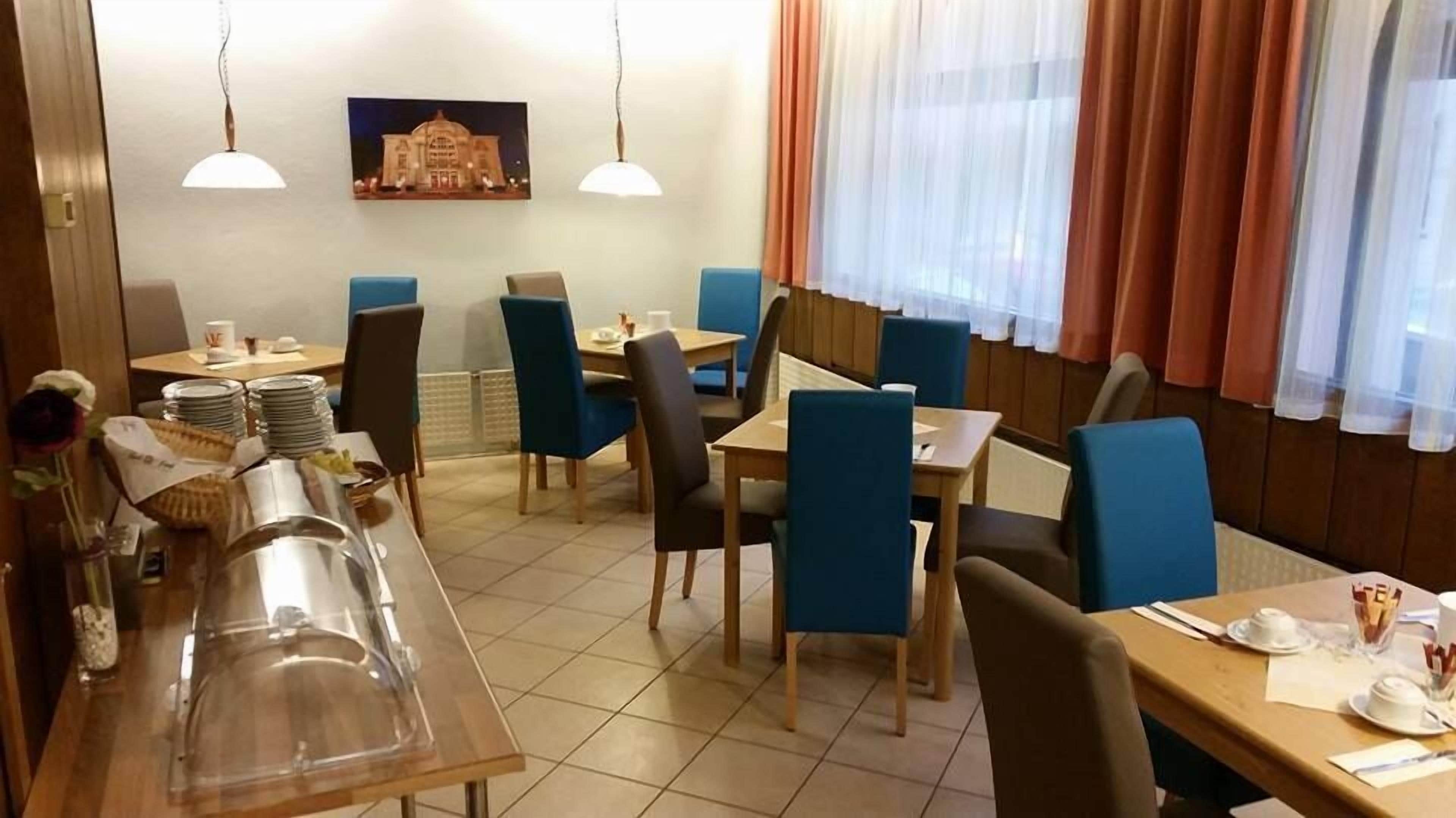 Ein Restaurant mit mehreren Tischen und Stühlen, einem Buffetbereich mit Tellern und Besteck sowie einem großen Fenster mit Vorhängen.