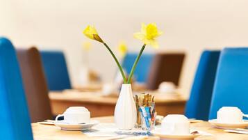 A dining table with a white vase containing yellow flowers, a glass of water, and a white cup and saucer.