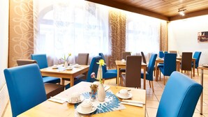 A restaurant with blue chairs and tables, a vase with flowers, and a patterned wall. - Altstadthotel Fürth (Fuerth)