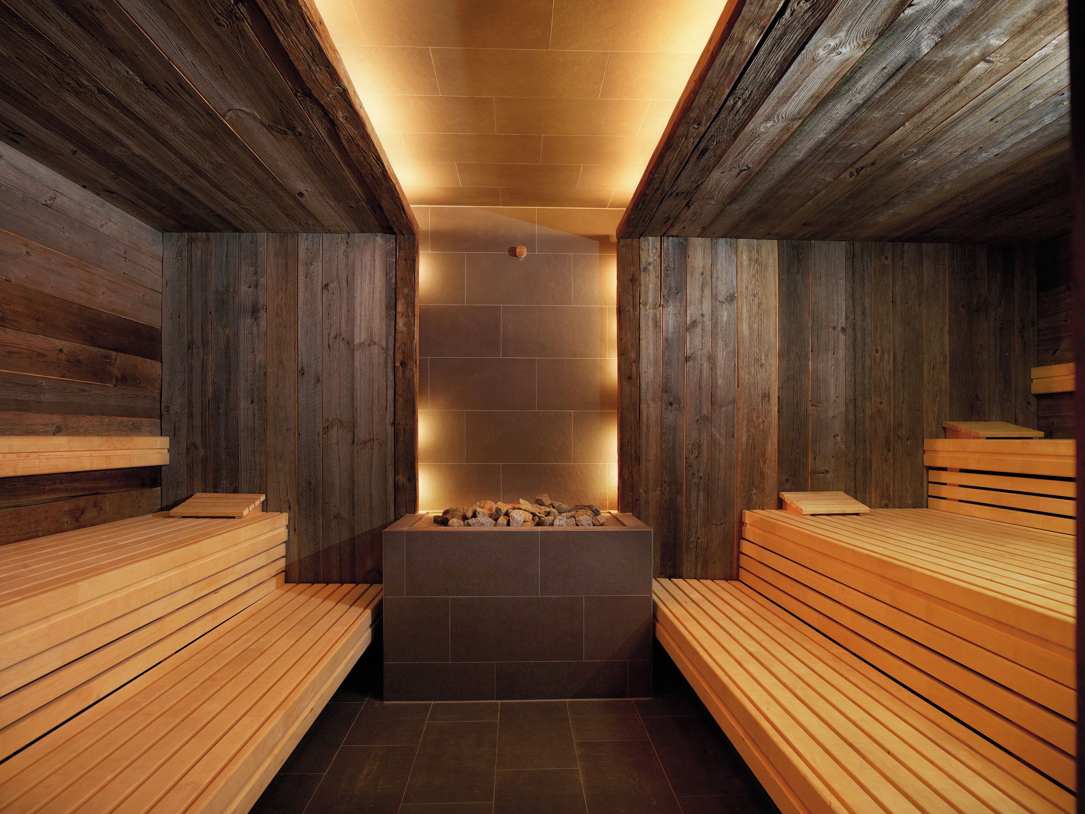 A sauna with wooden benches and a central heated stone area.