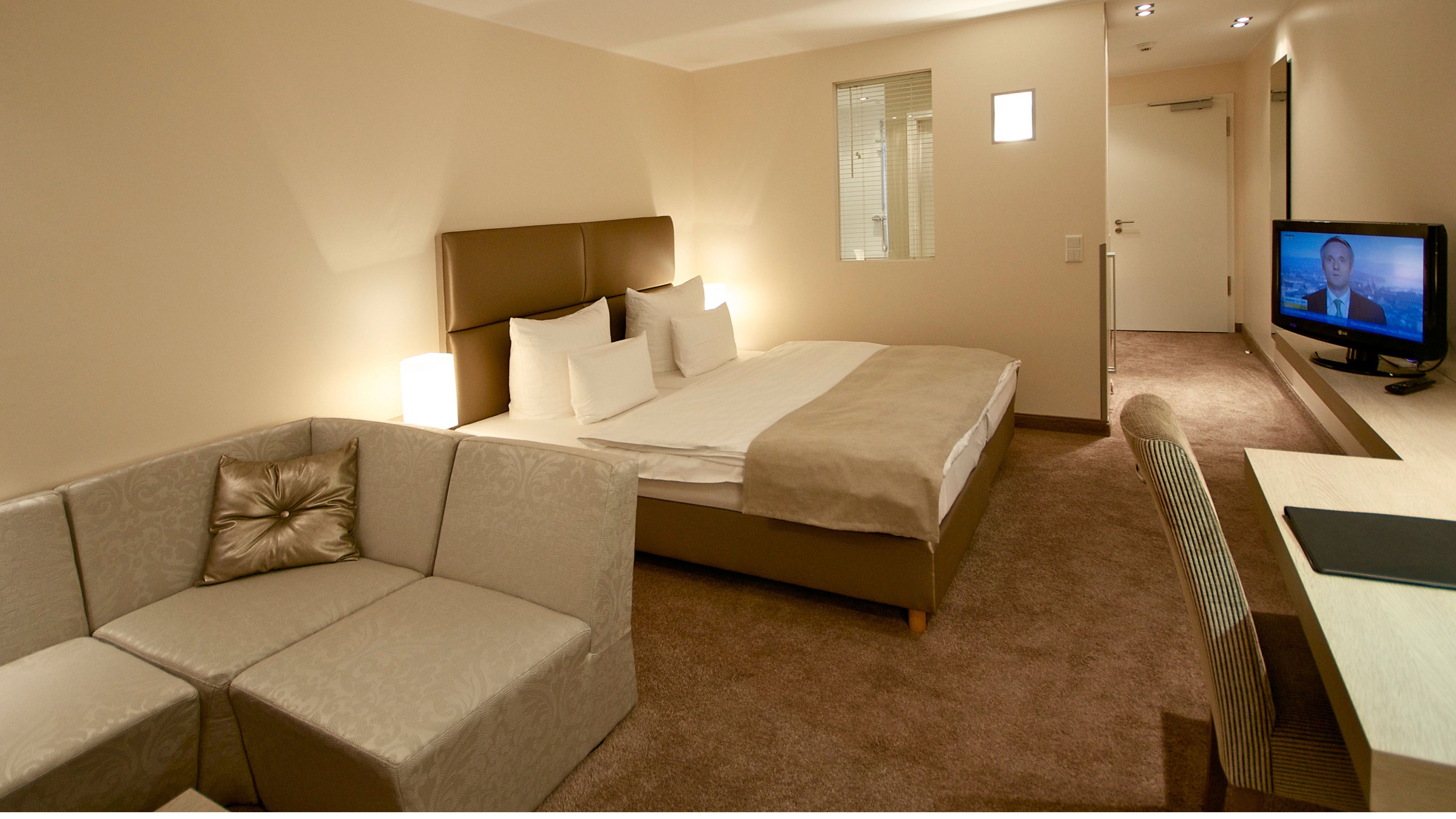 A hotel room with a bed, a sofa, a television, and a desk.