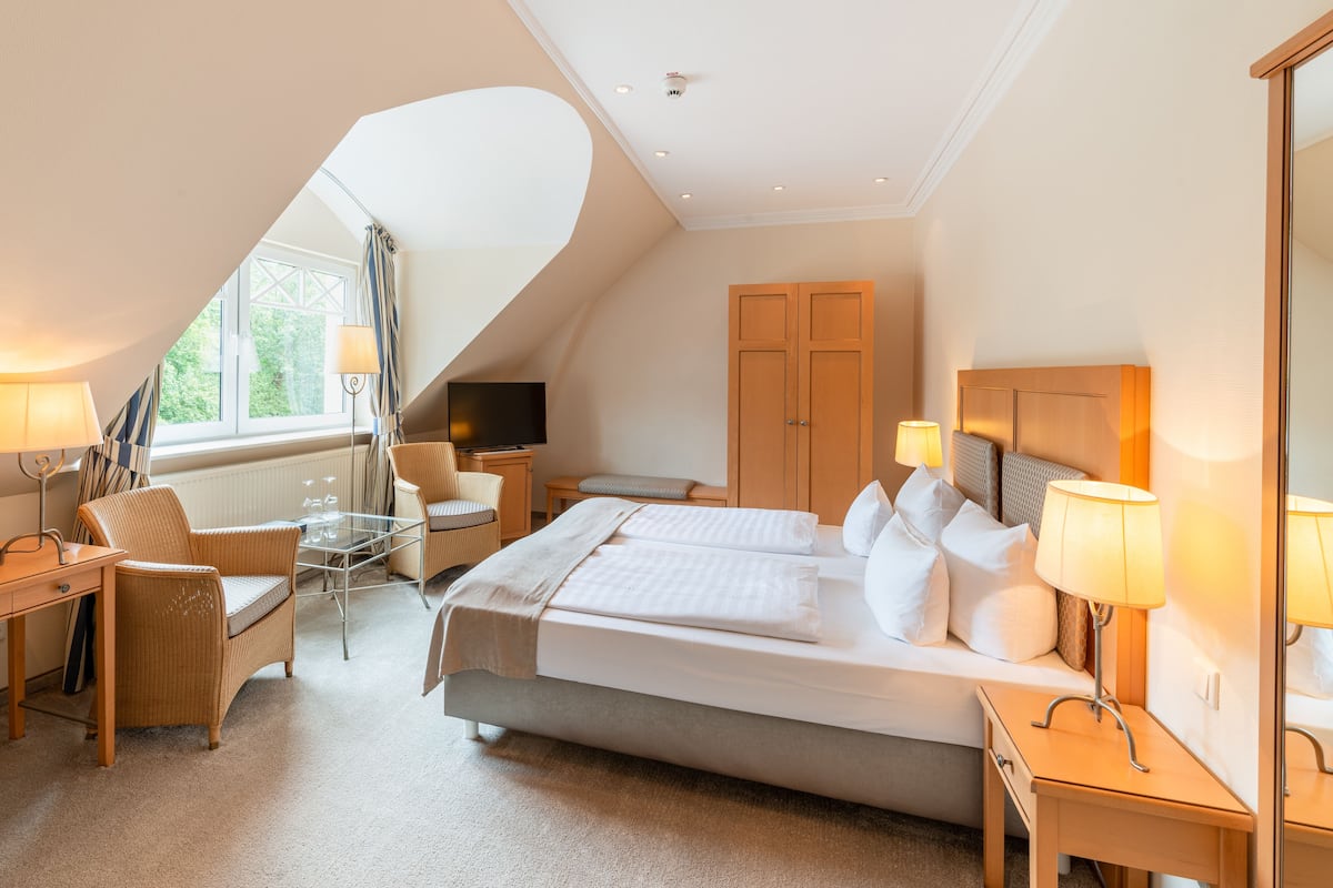 Ein Hotelzimmer mit einem großen Bett, einem Schreibtisch, einem Sessel, einem Fernseher und einem Fenster mit Vorhängen.